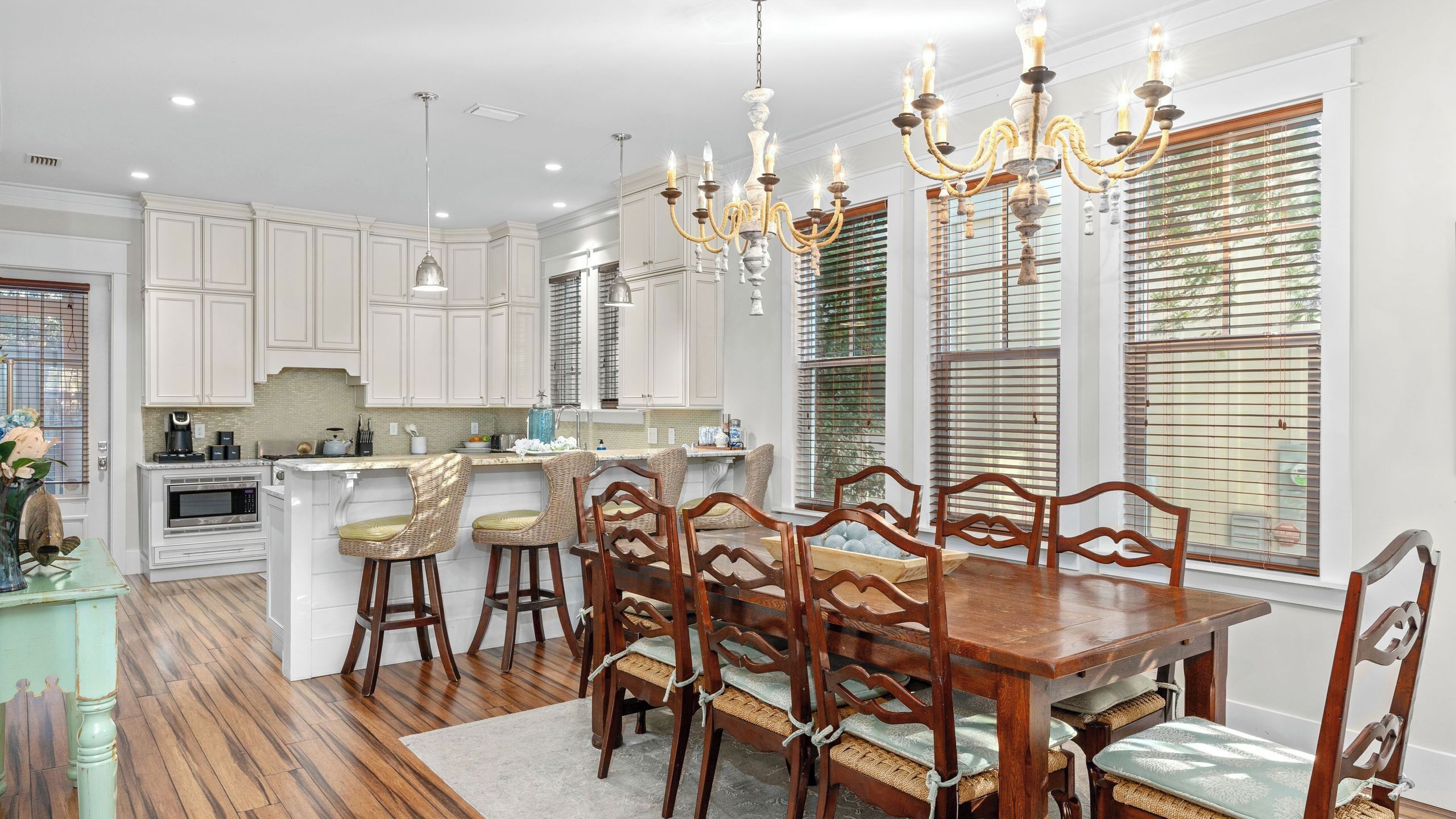 A modern kitchen with white cabinetry, a central island, bar stools, and a dining table with chairs.