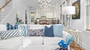 A spacious living room with a white sofa, patterned cushions, a chandelier, and a view into the kitchen. - Seagrove Gardens Mins to the Beach, Santa Rosa Retreat w/ A+ Design (Santa Rosa Beach)