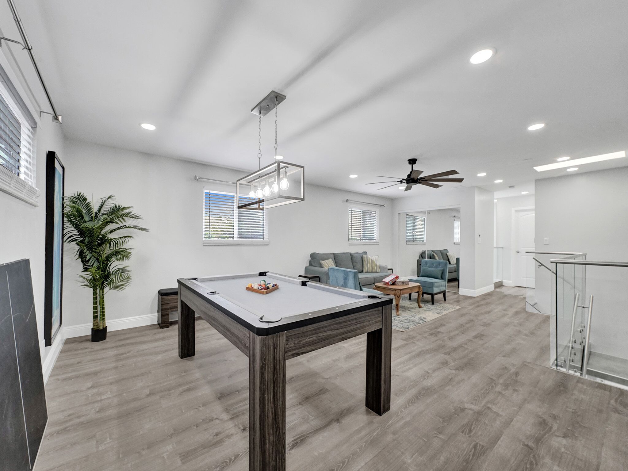 A spacious living area with a pool table, a ceiling fan, and a modern kitchen in the background.