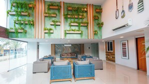 Un vestíbulo espacioso con techo alto, que presenta una pared verde con jardines verticales, una zona de estar con sofás azul y gris, y un suelo pulido.
