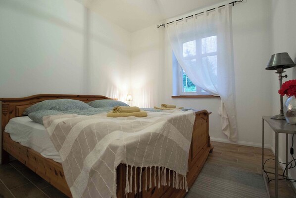 Une chambre à coucher avec un lit en bois, une table de chevet avec une lampe et une fenêtre ornée de rideaux légers.