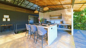 A modern kitchen with a central island, bar stools, and a hanging light fixture.