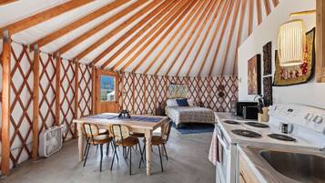 Un interior acogedor con una pared de celosía de madera, una mesa de comedor con sillas, una cama y una zona de cocina con estufa y fregadero.