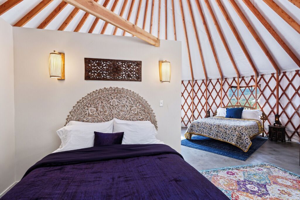 A room with a bed, a headboard, two wall sconces, a decorative panel, and a lattice wall.