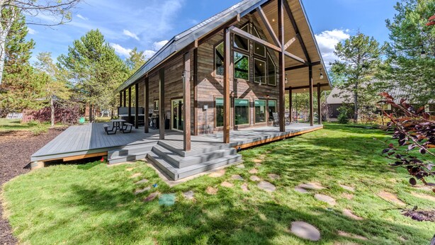A modern log cabin with a large deck, surrounded by a well-maintained lawn and trees. - 20+ Guests-20 Minutes to Yellowstone-Hot Tub-Family Reunions-Fly Fishing (Island Park)