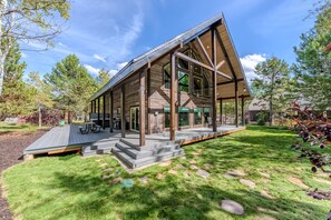 Une cabane en rondins moderne dotée d’une grande terrasse, entourée d’une pelouse bien entretenue et d’arbres.