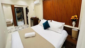 Camera d'albergo con un letto, una testiera in legno, un comodino con una lampada, un vaso con fiori e un bagno visibile attraverso una porta aperta.