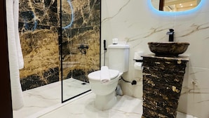 Un bagno moderno con pavimento in marmo, cabina doccia in vetro, WC bianco e lavabo con bacino in pietra.