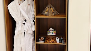 Un armadio in legno con ripiano superiore che contiene un cuscino, ripiano centrale con un oggetto decorativo e ripiano inferiore con una scatola e un telecomando.