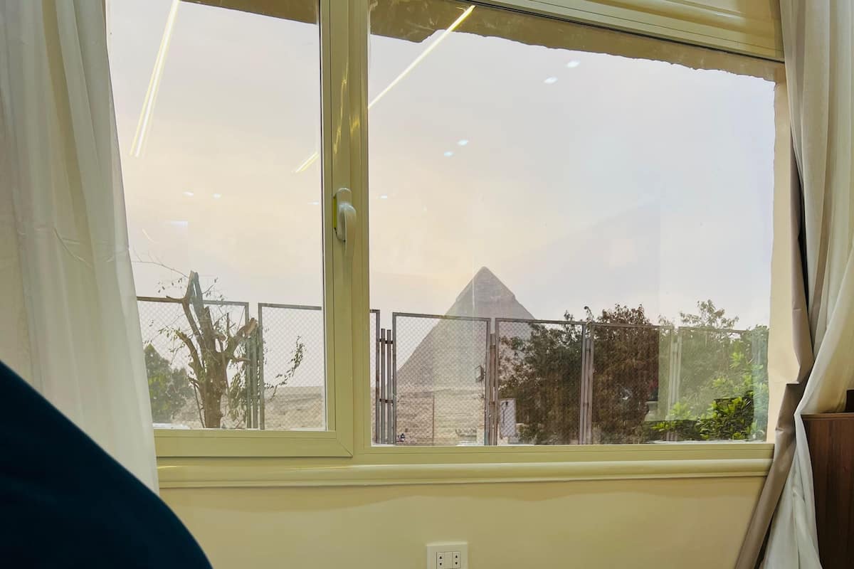 Ein Hotelzimmer mit einem Bett, einem Fenster mit Blick auf eine Pyramide und einem Vorhang.