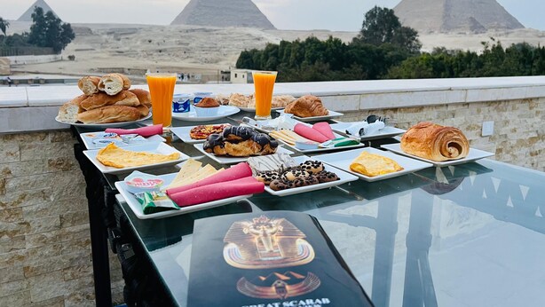 Una tavola imbandita per la colazione con dolci e bevande, con vista sulle piramidi.