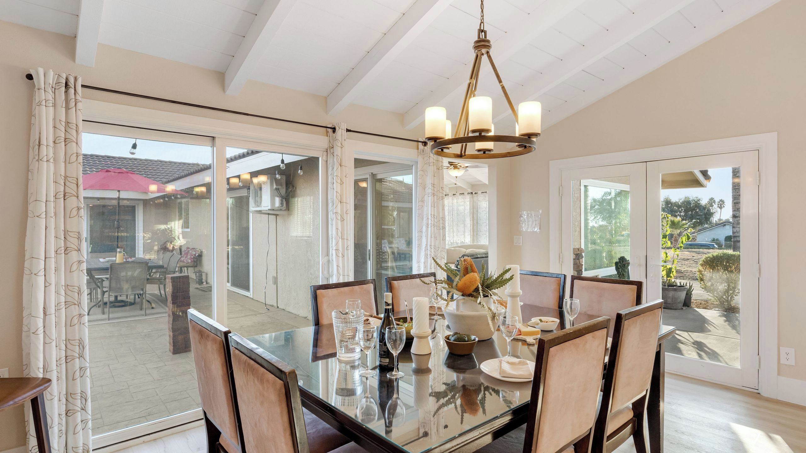 A dining area with a glass table, chairs, a chandelier, and a view of the outdoor patio.