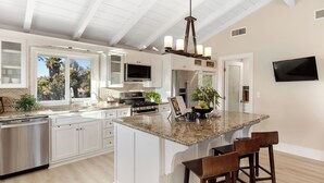 Una cocina moderna con muebles blancos, encimera de granito, estufa de acero inoxidable y televisor empotrado.