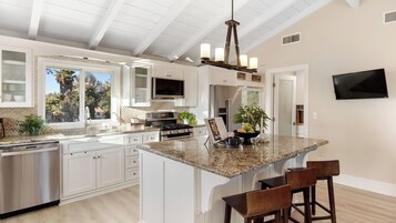 A modern kitchen with white cabinetry, a granite countertop, a stainless steel range, and a built-in TV.