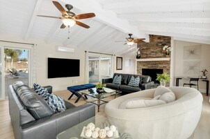 A spacious living room with a large sectional sofa, a round white chair, a glass coffee table, and two ceiling fans.