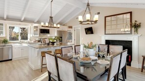 A modern kitchen with a central island, a dining area with a glass table, and a fireplace. - Bordeaux by Avantstay Private Pool, Hot Tub & Game Room Near Temecula (Temecula)