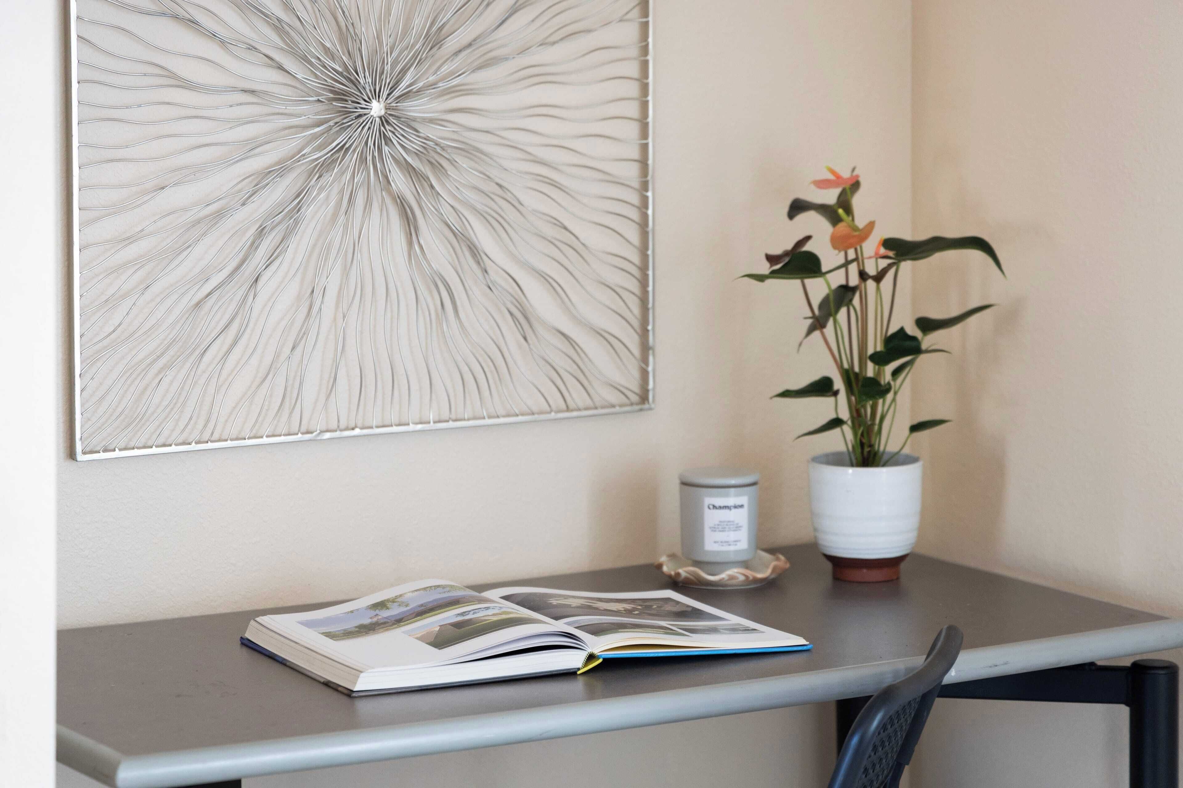 Una habitación con una mesa que tiene un libro, una planta en maceta y un tarro.