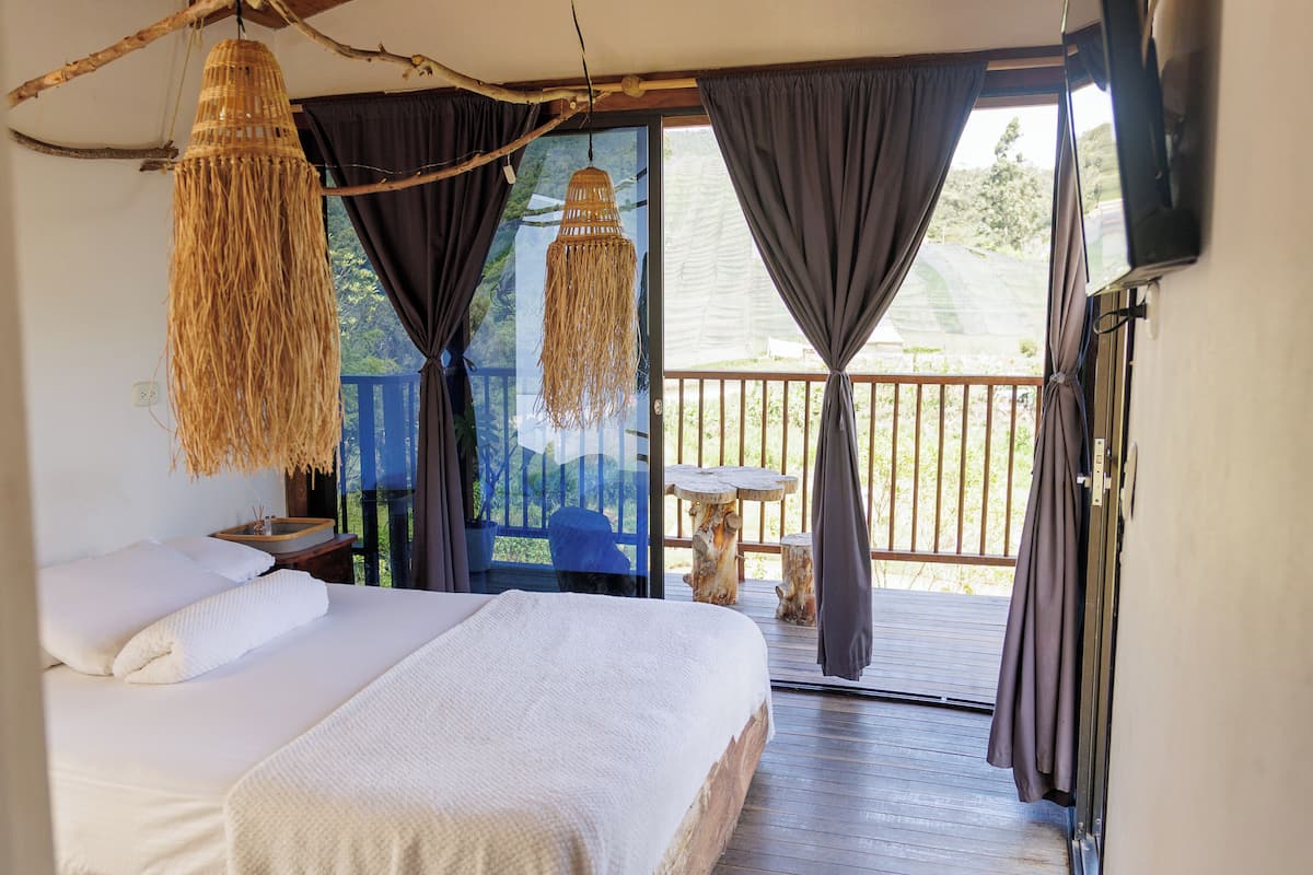 A bedroom with a large bed, a hanging light fixture, and a view of a balcony.