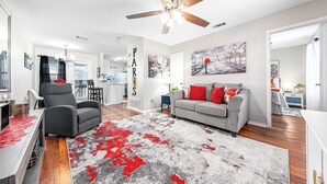 A spacious living room with a grey sofa, red cushions, and a red and grey rug. There is a ceiling fan, a dining table, and a kitchen in the background. - Charming 2-bedroom apartment with WiFi, AC in Killeen (Killeen)