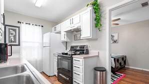 A modern kitchen with white cabinets, a stainless steel sink, a stove, and a trash can. - Charming 2-bedroom apartment with WiFi, AC in Killeen (Killeen)