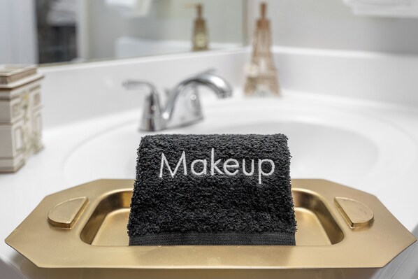 Ein Badezimmerwaschbecken mit einer goldfarbenen Spüle und einem schwarzen Handtuch mit dem Schriftzug 'Makeup'.