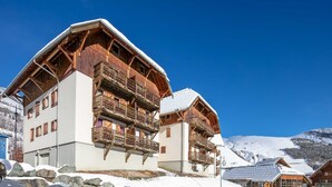A chalet-style building with wooden balconies and a snow-covered roof, set against a mountainous backdrop. - Wonderful appt 6 ppl with balcony (Saint-Sorlin-d´Arves)