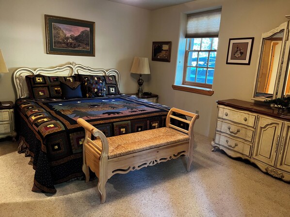 A bedroom with a large bed, a wooden chair, a dresser, and two framed pictures on the wall.