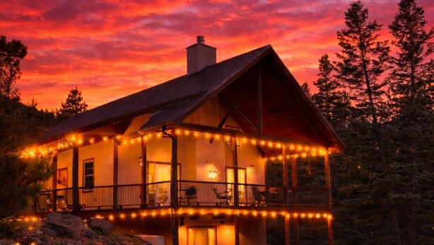 A cabin with a fire pit and red chairs, surrounded by a deck with string lights.
