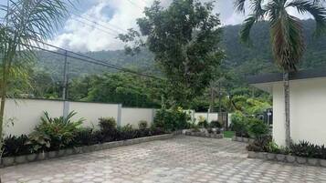 Pátio pavimentado com ladrilhos hexagonais, cercado por vegetação exuberante e palmeiras, com montanhas ao fundo.