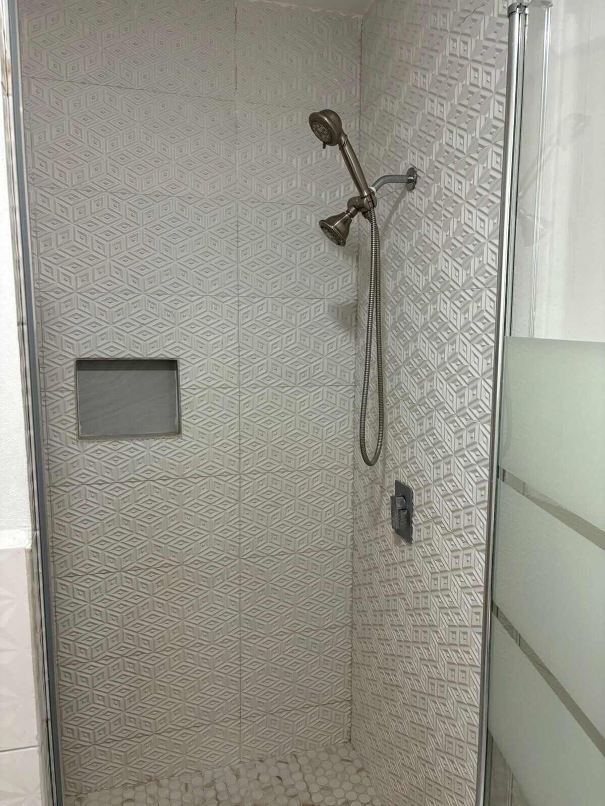Eine Dusche mit Wandpaneelen im geometrischen Muster, einer Handbrause und einer Bedienkonsole.