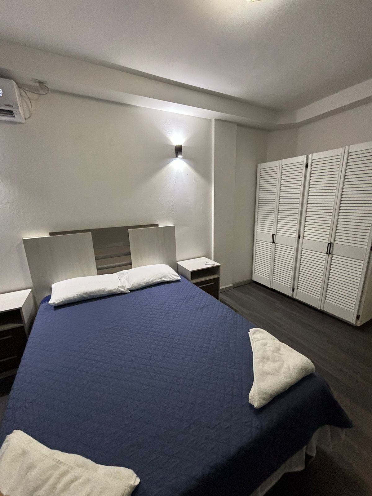 A bedroom with a bed, bedside tables, a wardrobe, and a wall-mounted light.
