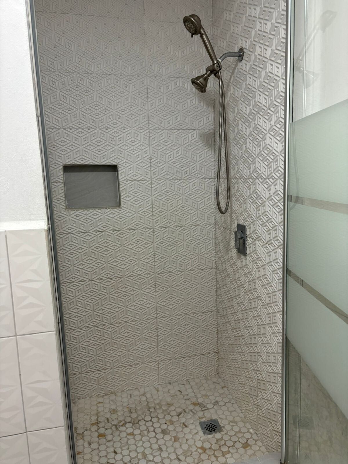 Una ducha con un diseño geométrico de azulejos, un cabezal de ducha manual y un desagüe.