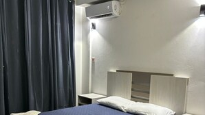 Een slaapkamer met een bed, nachtkastje, airconditioning aan de muur en een raam met gordijnen.