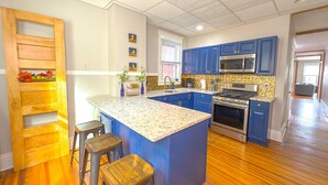 Una cocina con armarios azules, una isla central, taburetes de madera y un microondas.