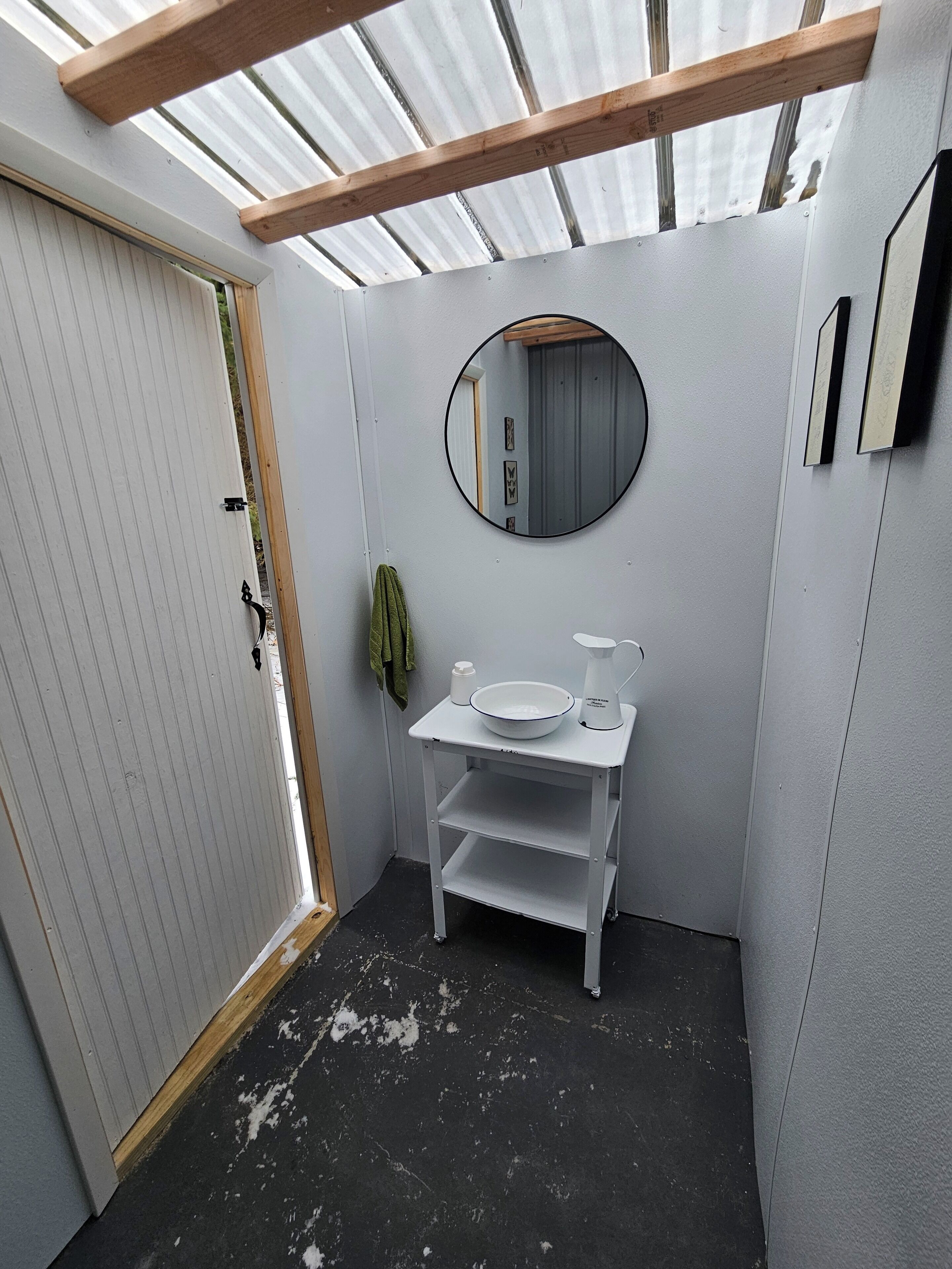 Een kleine badkamer met een wit wastafelmeubel, een ronde spiegel en een klein wastafel.