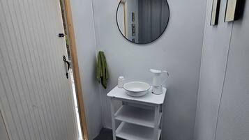 Een kleine badkamer met een wit wastafelmeubel, een ronde spiegel en een klein wastafel.