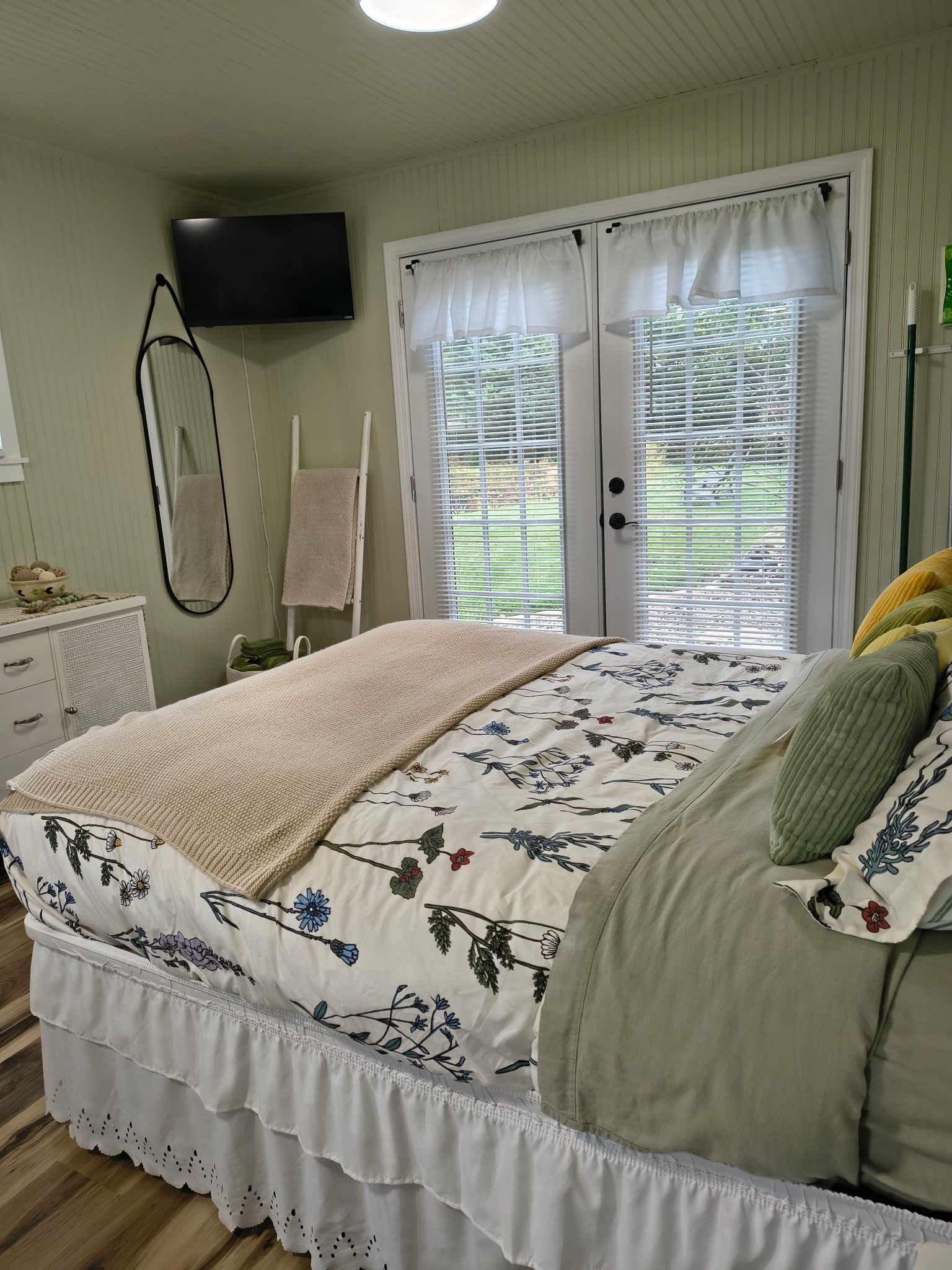 Een slaapkamer met een bed, een televisie, een raam met zonwering, een handdoekhouder en een nachtkastje.