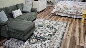A bedroom with a green sofa, a bed with floral bedding, a ceiling fan, and a large rug.