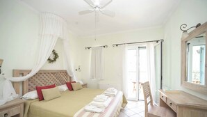 Une chambre à coucher comprenant un lit, un bureau, une chaise, un ventilateur de plafond et une fenêtre avec des rideaux.