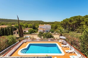 A swimming pool with lounge chairs and a view of a hillside with houses. - Villa Can Biel (Mercadal)