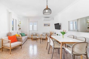 A bright, white interior with a sofa, chairs, a dining table, and a hanging light fixture. - Villa Can Biel (Mercadal)