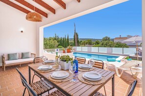 A terrace with a dining table set for six, a pool, and a view of the surrounding landscape. - Villa Can Biel (Mercadal)