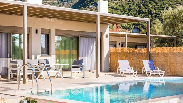 A modern outdoor pool area with lounge chairs and a covered seating area, surrounded by a mountain backdrop. - Villa Averto Anna (Lefkada)