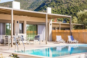 Zona de piscina moderna al aire libre con sillas de descanso y un área de estar cubierta, con montañas al fondo.
