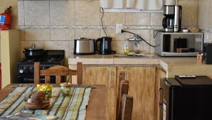 A kitchen with a stove, microwave, and coffee maker. There is a table with a placemat and a bowl of fruit. - Argentina, Mountain Lodge (El Calafate)