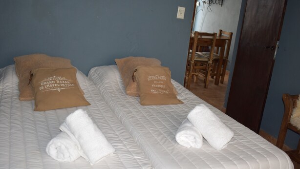 Two beds with white bedding and brown pillows, a wooden chair, and a door. - Argentina, Mountain Lodge (El Calafate)