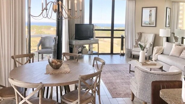Ein geräumiges Wohnzimmer mit großem Esstisch, bequemen Sitzgelegenheiten, einem Fernseher und Blick ins Freie.