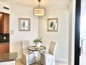 A modern living room with a round table, two chairs, a potted plant, and two framed wall art pieces.