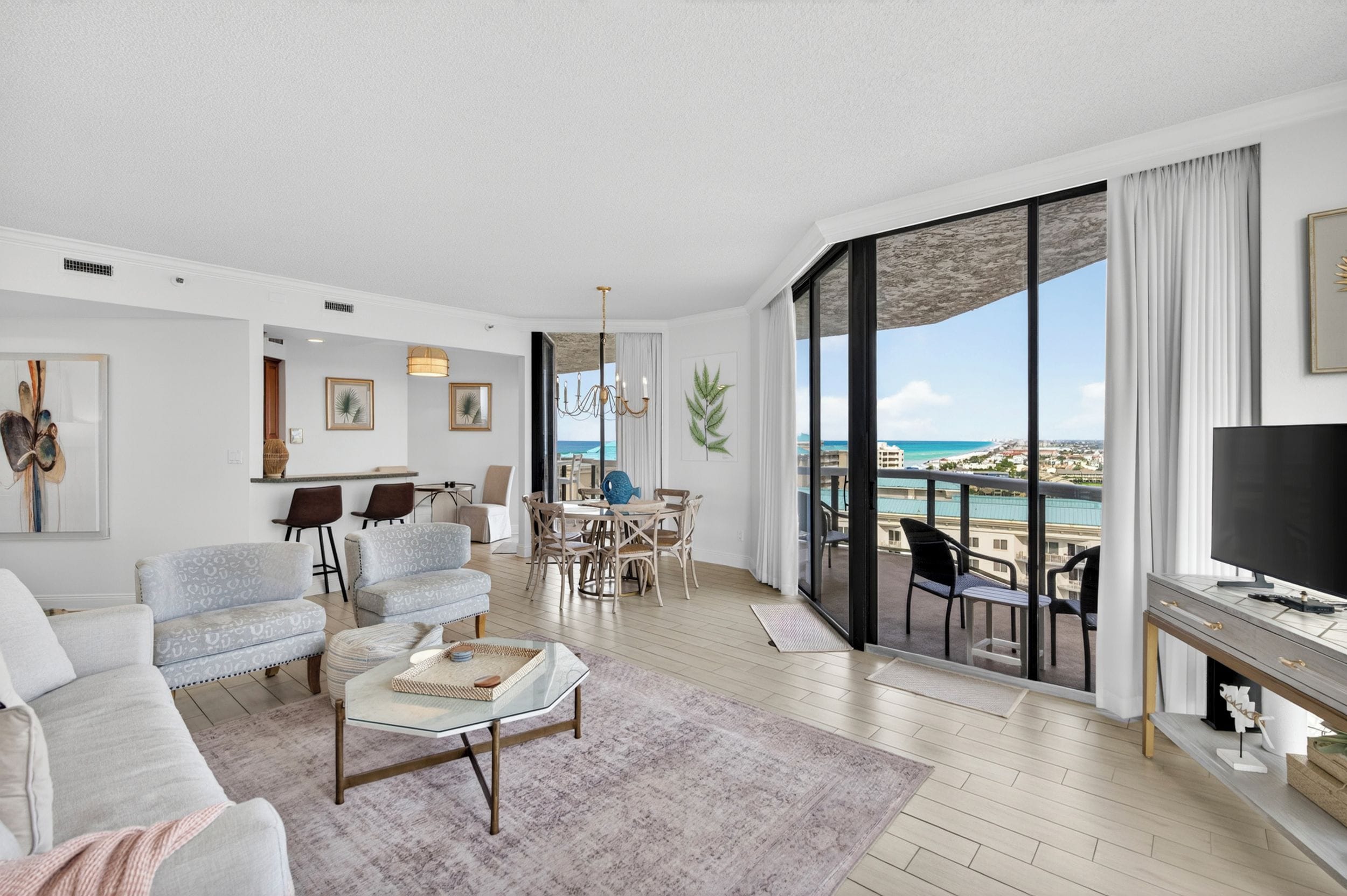 A spacious living room with a large window offering a view of the sea, a dining area with a view, and a flat-screen TV on a stand.