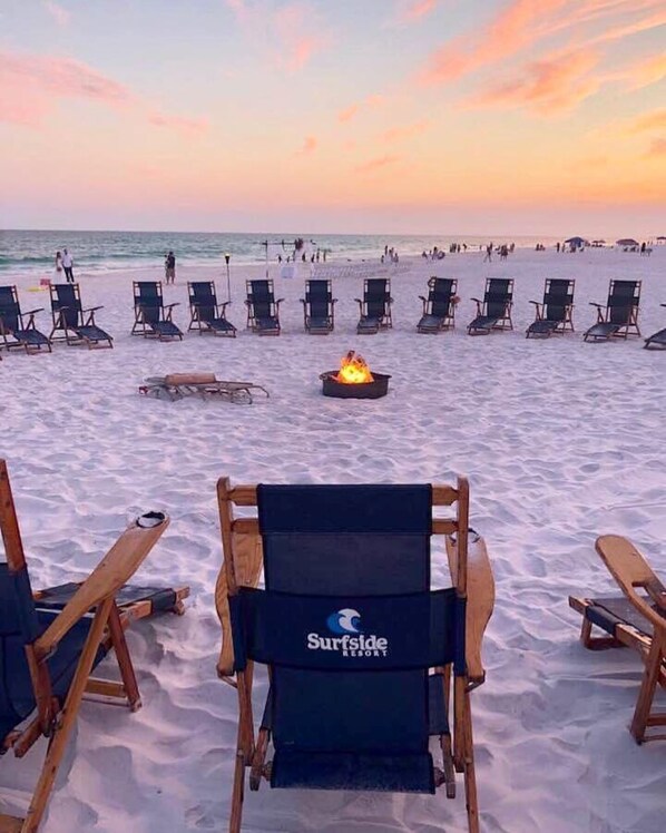 A beach with rows of lounge chairs and a fire pit in the center, with the logo 'Surfside Resort' on the back of one chair.